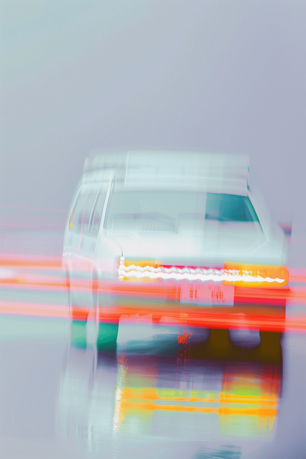 White car blurred by motion with red and orange light streaks on a wet road